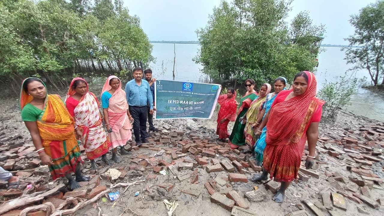 Village women gather on the shore with the "Ek Ped Maa Ke Naam" plantation banner