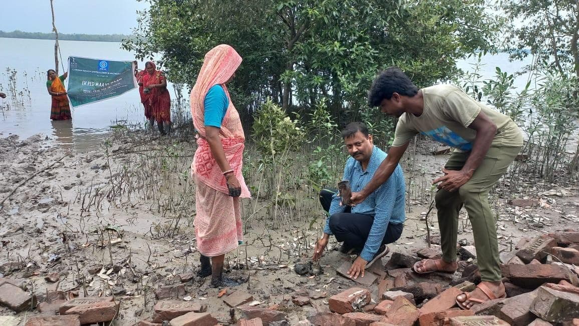 Planet Mama team members plant a sapling with women from the village