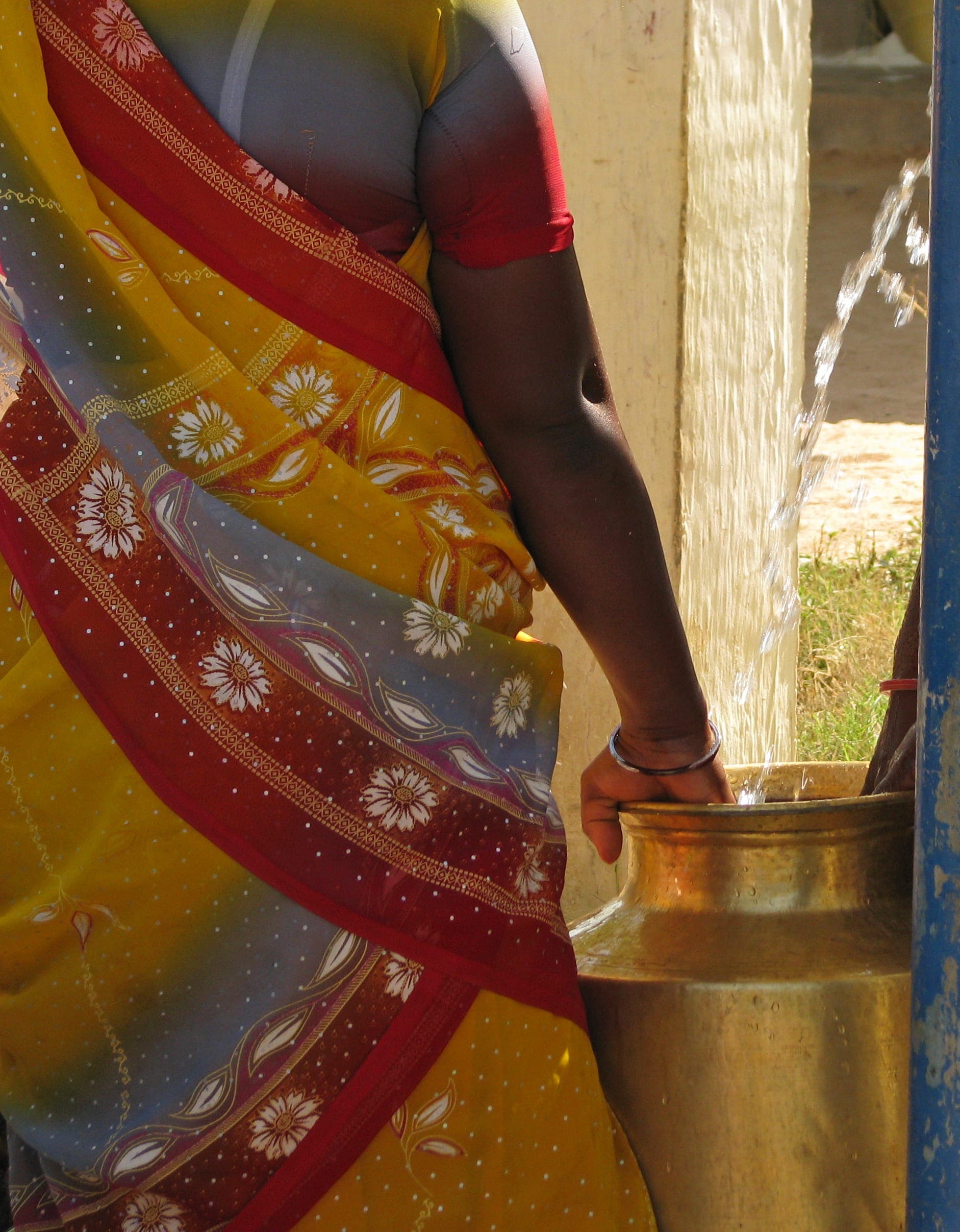 Close-up of a woman in a patterned sari filling a brass vessel with clear water